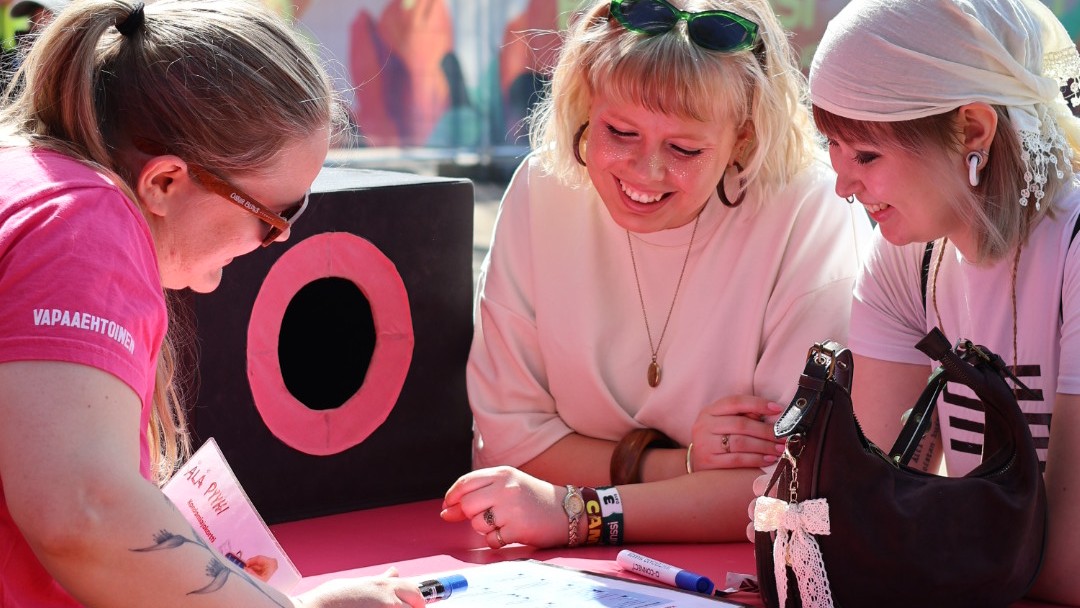 Kaksi nuorta aikuista ja vapaaehtoinen kesäkumikiskalla keskustelemassa kondomiajokortin teoriaosuudesta eli turvalliseen seksiin liittyvistä kysymyksistä.